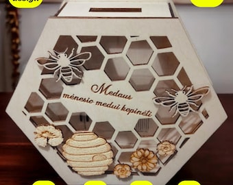 May include: A wooden hexagonal honey pot money box with a slot on the top. The box is decorated with a honeycomb pattern, bees, flowers, and the text "Medaus menesio medui kopineiti".