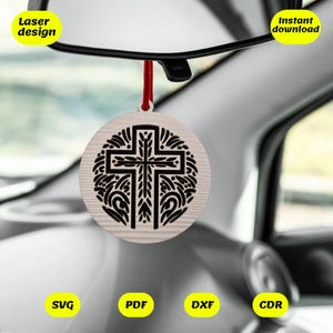 May include: A wooden car ornament featuring a black cross design. The cross is surrounded by a decorative floral pattern. The ornament is hanging from a red string.
