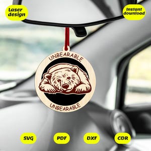 Puede incluir: Un adorno de coche de madera con una ilustración de un oso marrón y el texto "UNBEARABLE" sobre un fondo negro. El adorno está colgado de una cuerda roja.