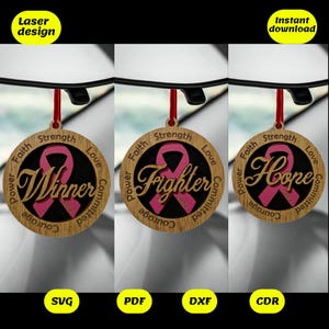 May include: Three wooden car ornaments with pink ribbon designs. The ornaments feature the words "Winner", "Fighter", and "Hope" with the year 2021 on the "Fighter" ornament. Each ornament has the words "Faith", "Strength", "Love", "Power", "Courage", and "Committed" around the ribbon.