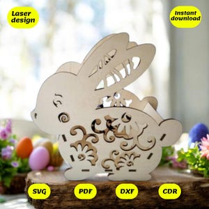 May include: Laser cut design of a wooden bunny with floral details. The bunny is holding a basket in its front paws. The design is available in SVG, PDF, DXF, and CDR formats. Instant download.