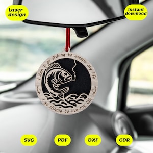 May include: A wooden car air freshener with a black and white design of a fish jumping out of the water. The text on the air freshener reads "I don't go fishing to escape my life I go fishing to live my life".