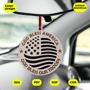 May include: A wooden car ornament with a red string for hanging. The ornament is round and features a black and white American flag with the text "God Bless America" and "God Bless Our Troops" around the flag.