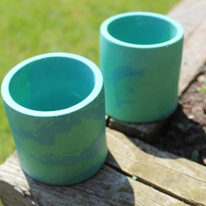 Könnte beinhalten: Zwei tealblaue Keramik-Blumentöpfe mit einem hellblauen Marmormuster. Die Töpfe stehen auf einer Holzoberfläche.