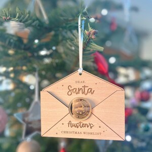 May include: A wooden Christmas ornament shaped like an envelope with a gold coin attached. The envelope says "Dear Santa" and "Austen's Christmas Wishlist". The coin has a reindeer and says "North Pole Santa Express".