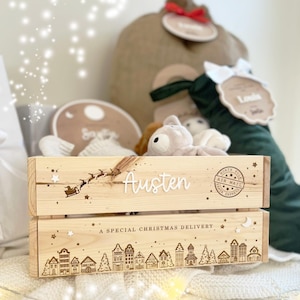 May include: A light-colored wooden crate featuring the name Austen in white script, a silhouette of Santa's sleigh, and a North Pole Air Mail stamp. The bottom panel displays a village scene with the text A SPECIAL CHRISTMAS DELIVERY.