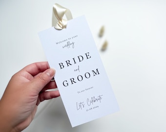 May include: A white wedding sign with black text that reads "Welcome to your wedding", "BRIDE and GROOM", "To our forever", and "Let's Celebrate 31.08.2024". The sign is held by a hand and has a cream ribbon.
