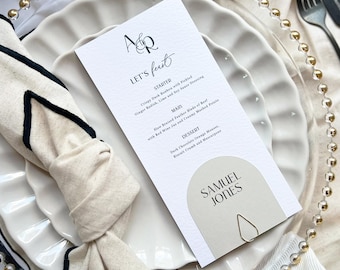 May include: A white card with a menu for a wedding reception. The menu includes a starter, main course, and dessert. The card is on a white plate with a gold beaded rim. The card has the text "A&R Let's Feast" at the top.