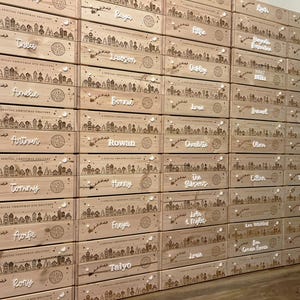 May include: A stack of rectangular light-colored wooden crates, each featuring a laser-engraved winter village scene with a flying sleigh and the text A SPECIAL CHRISTMAS DELIVERY. Each crate is personalized with a white script name attached.