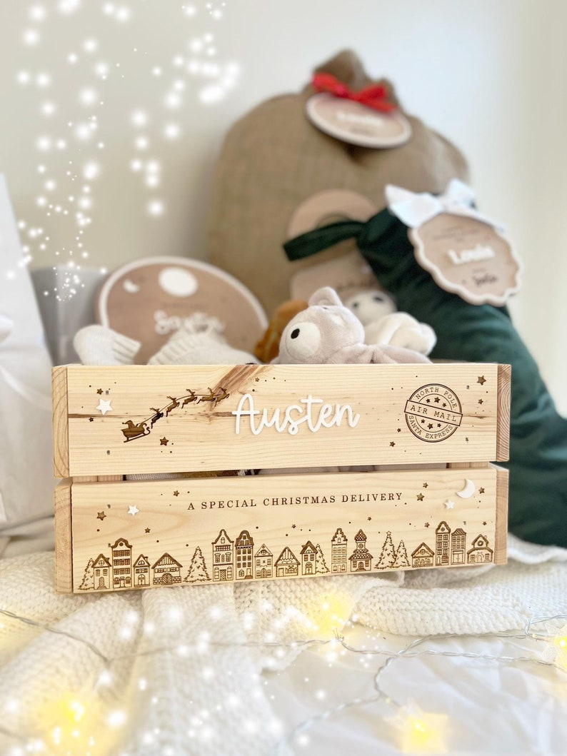 May include: A light-colored wooden crate featuring the name Austen in white script, a silhouette of Santa's sleigh, and a North Pole Air Mail stamp. The bottom panel displays a village scene with the text A SPECIAL CHRISTMAS DELIVERY.