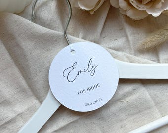 May include: White wooden hanger with a round tag that says "Emily The Bride 29.03.2025".