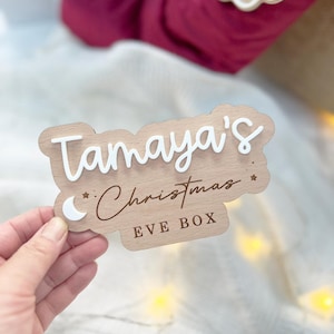May include: A wooden Christmas Eve box with the name "Tamaya's" and the text "Christmas Eve Box" in white lettering. A crescent moon and stars are also included in the design.
