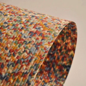 May include: A close-up of a sheet of paper with a colorful, textured pattern. The pattern is made up of small, irregular shapes in shades of red, orange, yellow, green, blue, and beige. The paper is curved, showing its thickness and texture.
