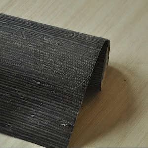 May include: A roll of black textured wallpaper with a subtle woven pattern. The wallpaper is rolled up and the edge is visible.