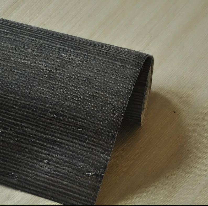 May include: A roll of black textured wallpaper with a subtle woven pattern. The wallpaper is rolled up and the edge is visible.