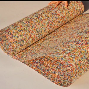 May include: A roll of colorful, patterned paper with a mosaic-like design. The paper features a mix of red, blue, yellow, and green hues, creating a textured appearance. The paper is being unrolled, revealing its full pattern.
