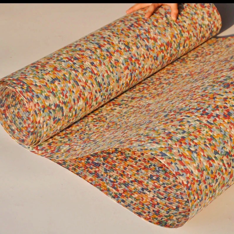 May include: A roll of colorful, patterned paper with a mosaic-like design. The paper features a mix of red, blue, yellow, and green hues, creating a textured appearance. The paper is being unrolled, revealing its full pattern.