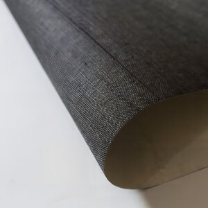 May include: Close-up of a dark gray fabric with a textured weave. The fabric is folded over, revealing a lighter beige underside.