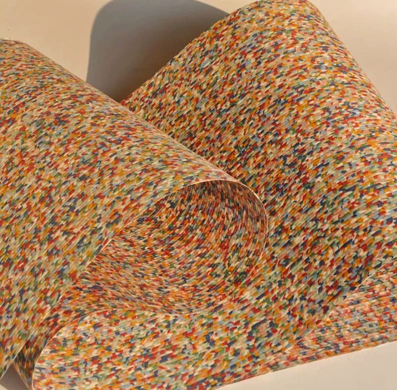 May include: Rolled paper with a colorful, speckled pattern. The design features a mix of red, blue, yellow, and green dots, creating a textured appearance. The paper is curled, revealing the pattern on the inside.