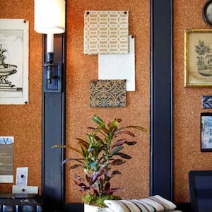May include: A corkboard with various fabric swatches, a framed print, and a potted plant. The corkboard is mounted on a black wall. A stack of folded fabric is on a dark surface.