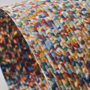 May include: A curved sheet of paper with a colorful, textured pattern. The design features a mosaic of small, irregular shapes in shades of red, blue, yellow, and green, creating a vibrant, abstract effect. The paper appears to have a woven or textured surface.