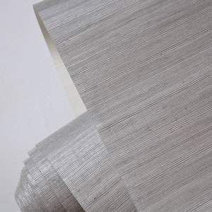 May include: A roll of silver metallic wallpaper with a subtle woven texture. The wallpaper has a slightly shimmery finish.