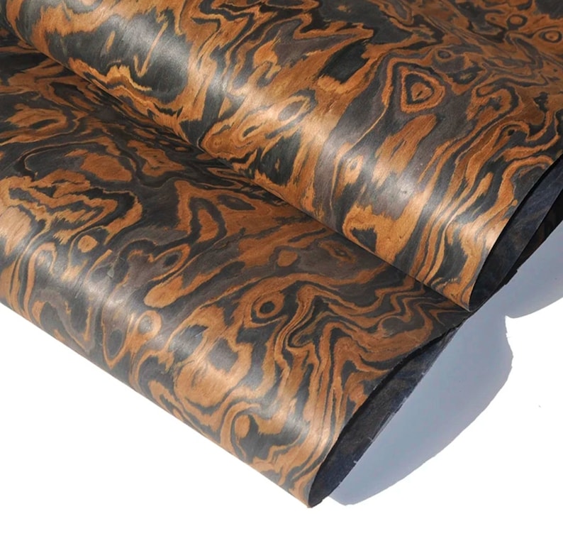 May include: Close-up of a sheet of wood veneer with a distinctive brown and black wood grain pattern. The wood has a swirling, marbled appearance.