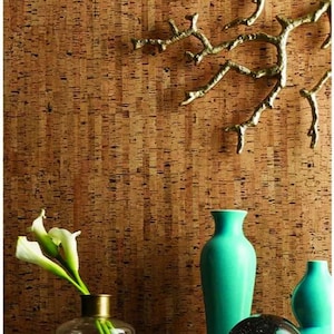 May include: A cork wall with a gold metal branch wall decor, a teal blue vase, a clear glass vase with white flowers, a clear glass orb, and a stack of books with the title "Francis Picabia" on the top book.