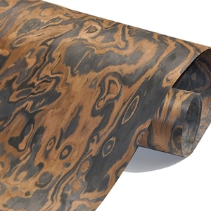 May include: A close-up of a sheet of wood veneer with a dark brown and black wood grain pattern. The veneer is rolled up and the edges are visible.