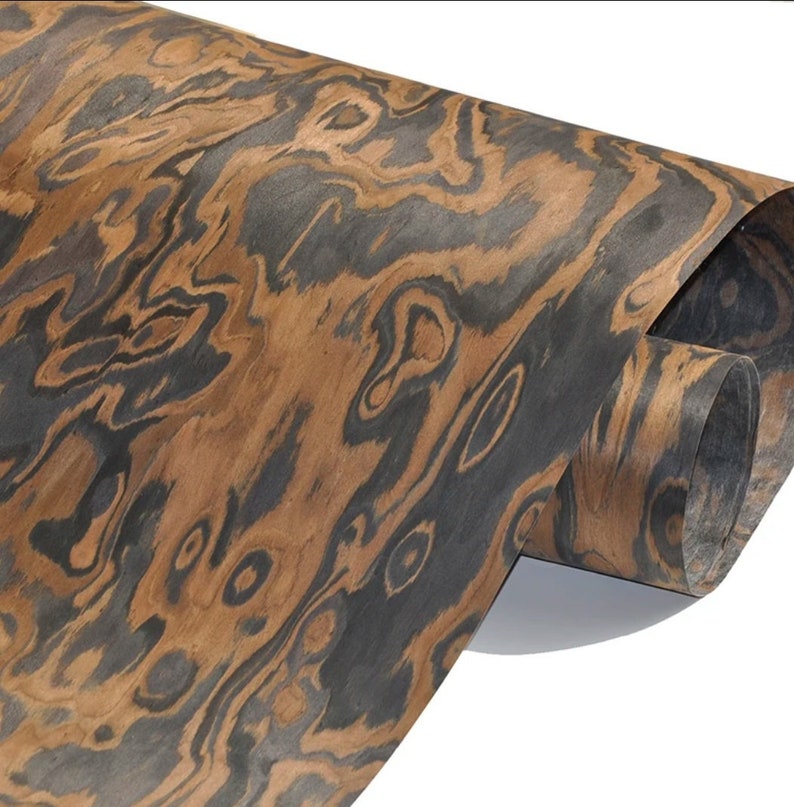 May include: A close-up of a sheet of wood veneer with a dark brown and black wood grain pattern. The veneer is rolled up and the edges are visible.