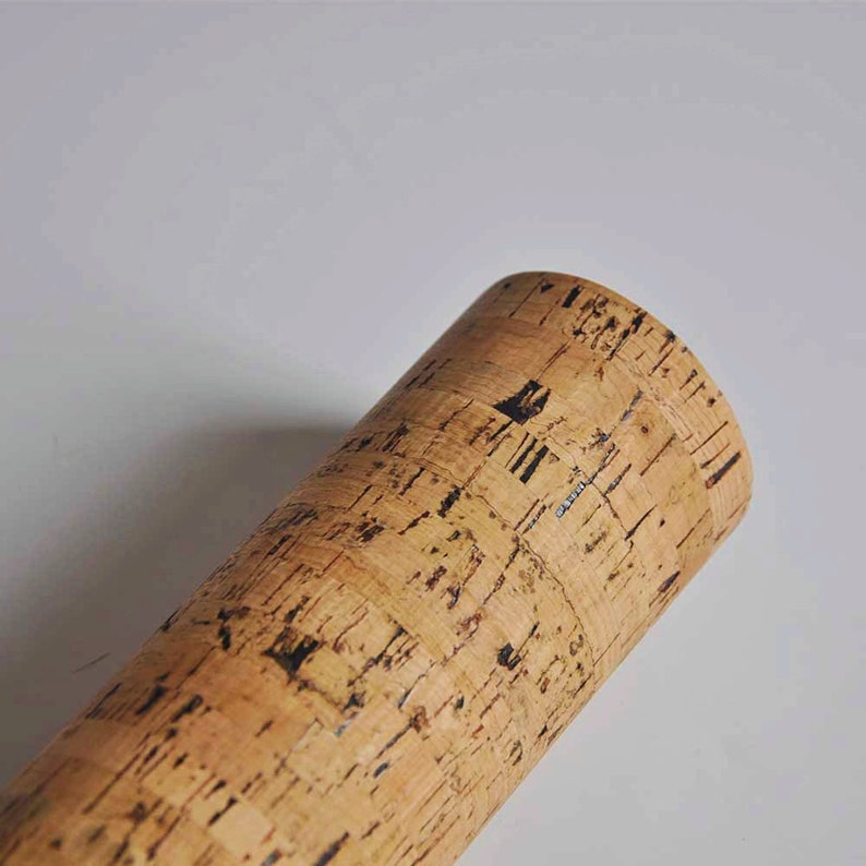 May include: Close-up of a cork rod with a natural brown colour and a black pattern. The cork is textured and has a rough surface.