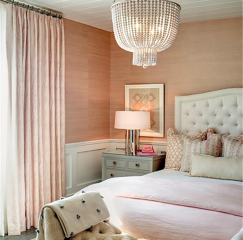 Puede incluir: Un dormitorio rosa con una cabecera capiton&eacute; blanca, una colcha rosa y una mesita de noche blanca con una l&aacute;mpara. La habitaci&oacute;n tiene un papel tapiz estampado en rosa y blanco y una gran l&aacute;mpara de ara&ntilde;a.