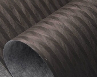 May include: Close-up of a dark gray, textured paper with a chevron pattern. The paper is rolled up and the texture is visible.