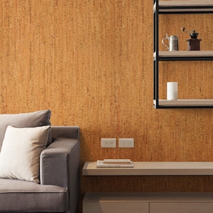 May include: A grey sofa with a white cushion sits in front of a wall covered in cork tiles. A floating shelf with two drawers is below the sofa. The shelf has a wooden top and two white electrical outlets are on the wall behind it.