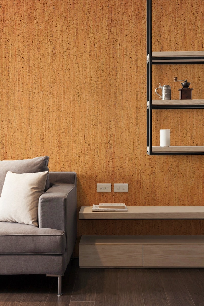 May include: A grey sofa with a white cushion sits in front of a wall covered in cork tiles. A floating shelf with two drawers is below the sofa. The shelf has a wooden top and two white electrical outlets are on the wall behind it.