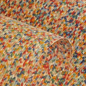 May include: Close-up of a sheet of paper with a colorful, abstract pattern. The design features small, irregular shapes in shades of red, blue, yellow, and green, creating a textured appearance. The paper is slightly curled, revealing the underside.
