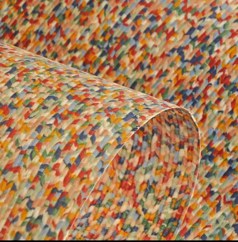 May include: Close-up of a sheet of paper with a colorful, abstract pattern. The design features small, irregular shapes in shades of red, blue, yellow, and green, creating a textured appearance. The paper is slightly curled, revealing the underside.