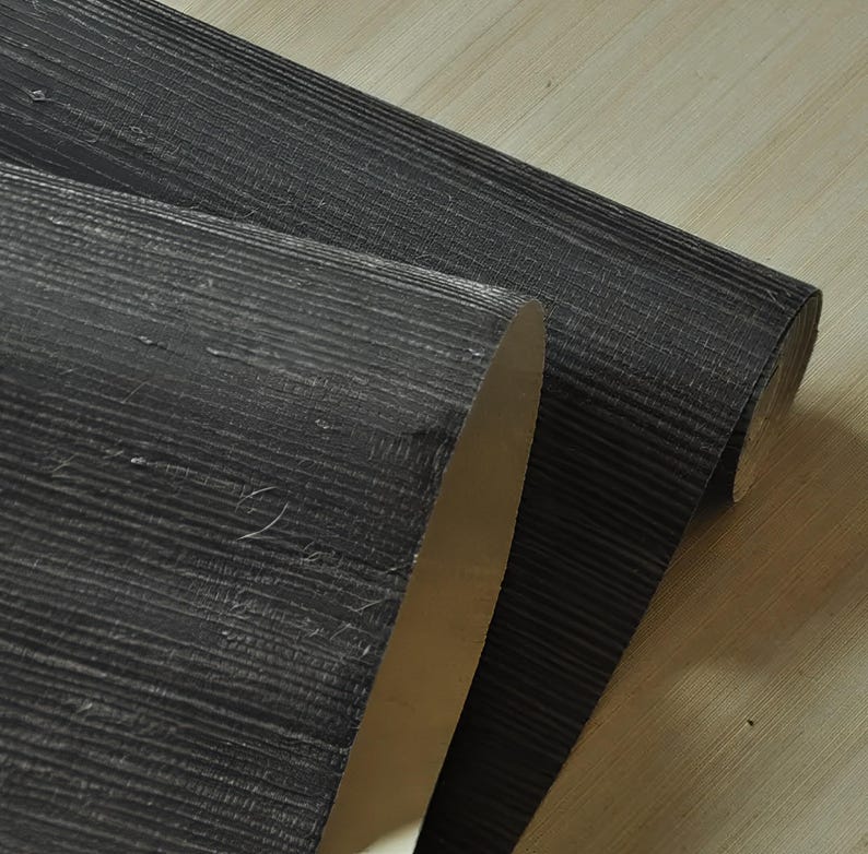 May include: A roll of black textured wallpaper with a subtle wood grain pattern.