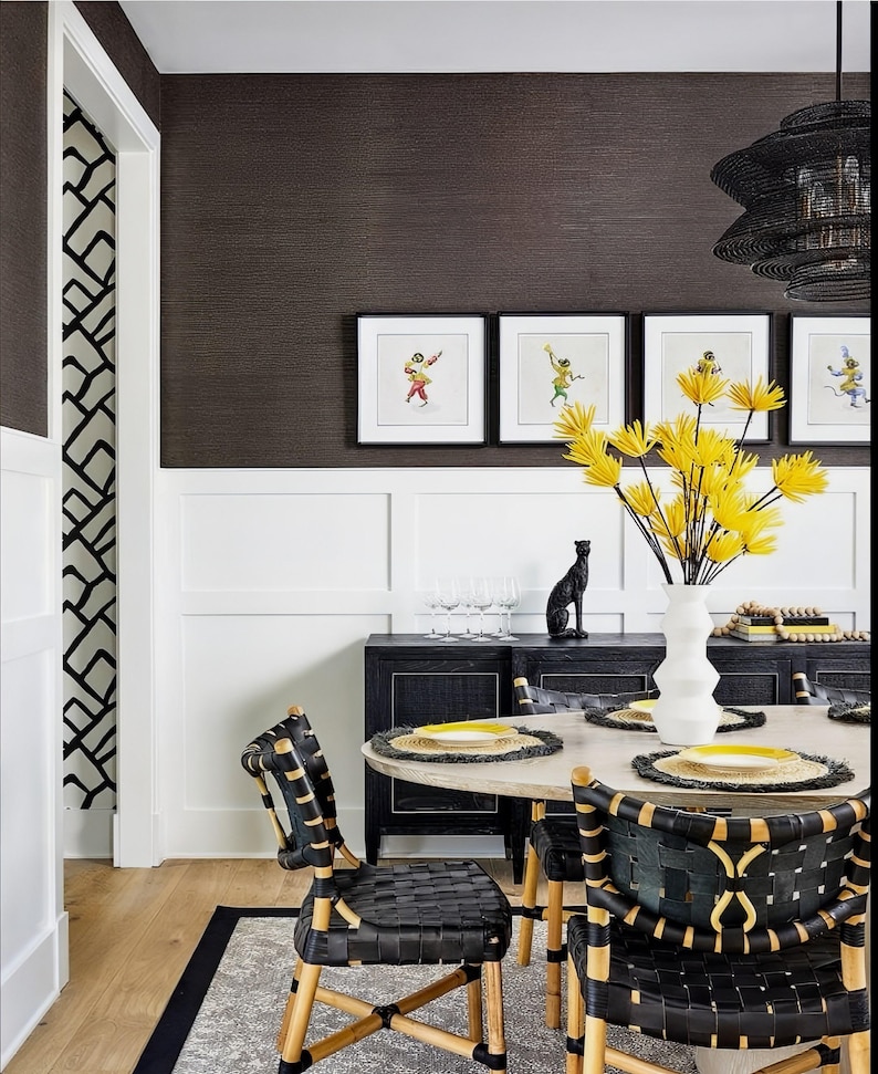 May include: A dining room with a black and white patterned wallpaper, a black and white patterned rug, a black table with a round top, and black chairs with woven seats. The table is set with yellow placemats and yellow plates. There are four framed pictures on the wall above the table.