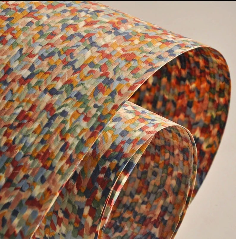 May include: Close-up of colorful patterned paper with a watercolor effect. The paper has a repeating design of small, irregular shapes in shades of red, blue, yellow, and green. The paper is curled, showing the pattern on both sides.