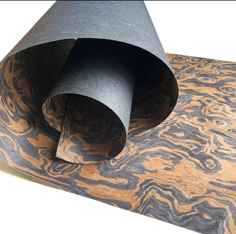 May include: A sheet of wood veneer with a dark brown and black wood grain pattern. The veneer is rolled up and the end of the roll is visible.