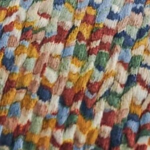 May include: Close-up of a colorful, textured rug. The rug features a pattern of interwoven threads in various colors, including red, blue, yellow, green, and white. The design is abstract and appears to be made of tightly packed, irregular shapes.