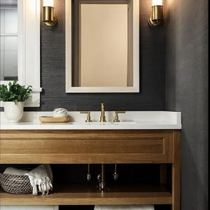 May include: A bathroom vanity with a white countertop and a wooden cabinet with open shelves. The vanity has a gold faucet and two gold wall sconces with frosted glass shades. The walls are dark gray and the shelves are filled with white towels.