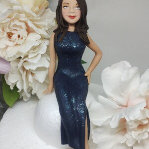 May include: A dark blue sparkly dress with a slit up the leg, worn by a woman with long brown hair and a neutral expression. She is sitting on a white round surface.