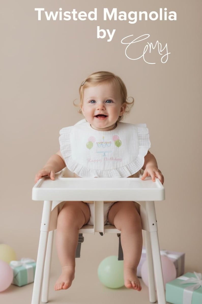 May include: A white ruffled bib featuring an embroidered birthday cake with pink and green balloons and the text Happy Birthday. The bib is worn by a child sitting in a white high chair. The image includes the text Twisted Magnolia by Amy.