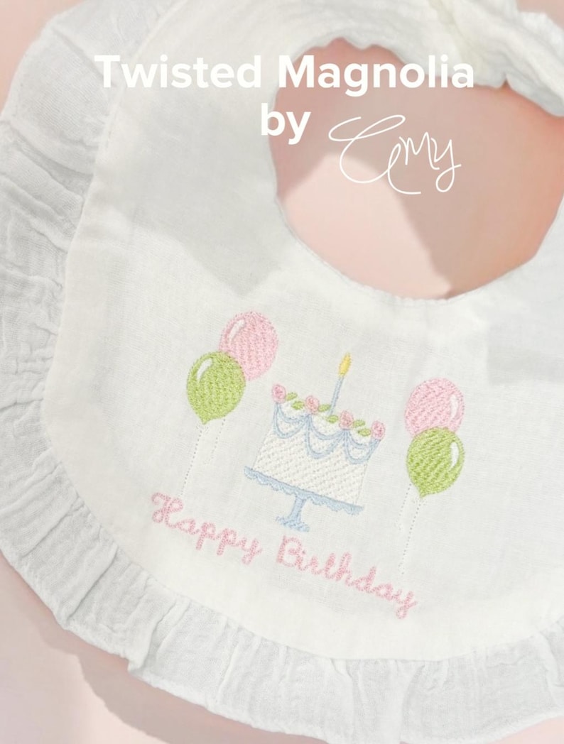 May include: A white ruffled baby bib featuring embroidered text that reads Twisted Magnolia by Cmy. The center design includes a birthday cake with a single candle, flanked by pairs of pink and green balloons, with the words Happy Birthday below.