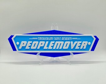 May include: A blue and white sign with the text "Tomorrowland Transit Authority" and "Peoplemover" in white lettering.