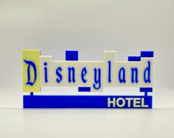 May include: A blue and white sign with the text "Disneyland Hotel" in a white font. The sign is made of plastic and has a 3D effect.