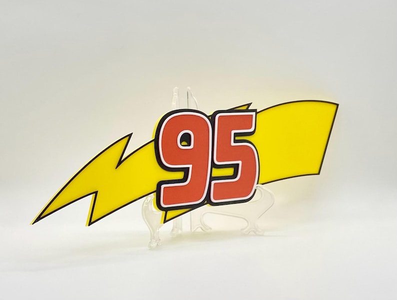 Puede incluir: Un rayo amarillo con el n&uacute;mero 95 en rojo y contorno negro. El n&uacute;mero est&aacute; sobre una bandera amarilla. El dise&ntilde;o est&aacute; sobre un soporte transparente.