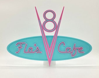 May include: A turquoise blue oval sign with a pink stylized 'V' and the number '8' in the center. The sign reads "Flo's Cafe" in pink script.